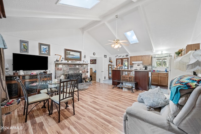 living room featuring light hardwood / wood-style floors, ceiling fan, high vaulted ceiling, a skylight, and a fireplace