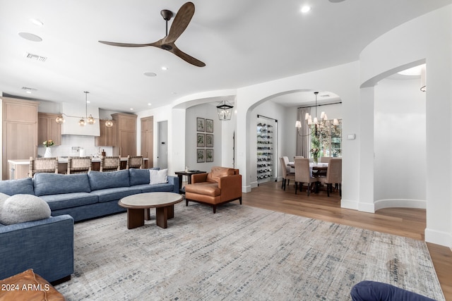 living room featuring ceiling fan with notable chandelier and light hardwood / wood-style flooring