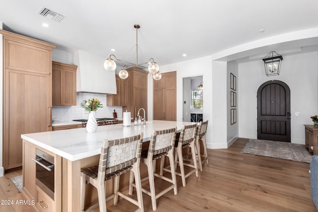 kitchen featuring a large island, stainless steel appliances, light hardwood / wood-style floors, decorative light fixtures, and decorative backsplash