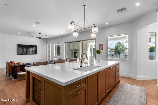 kitchen featuring ceiling fan with notable chandelier, sink, light wood-type flooring, an island with sink, and decorative light fixtures