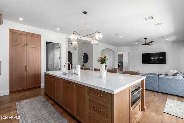 kitchen with ceiling fan with notable chandelier, light hardwood / wood-style floors, sink, and an island with sink