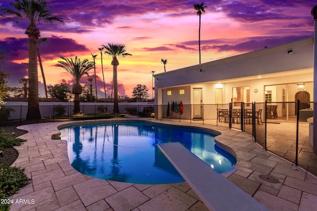 pool at dusk with a diving board and a patio