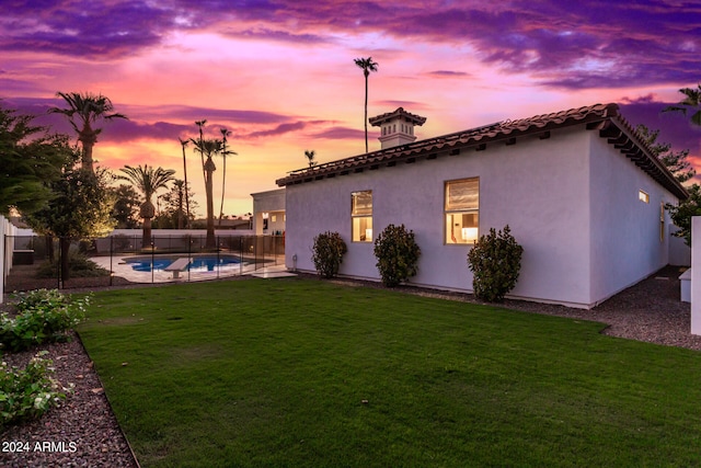 back house at dusk featuring a lawn and a fenced in pool