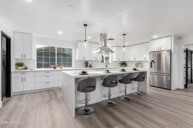 kitchen featuring a center island, island exhaust hood, pendant lighting, high quality fridge, and white cabinets