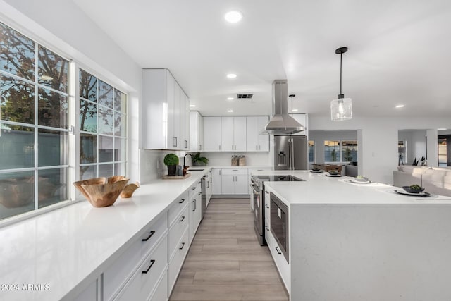 kitchen with appliances with stainless steel finishes, island range hood, sink, pendant lighting, and white cabinets