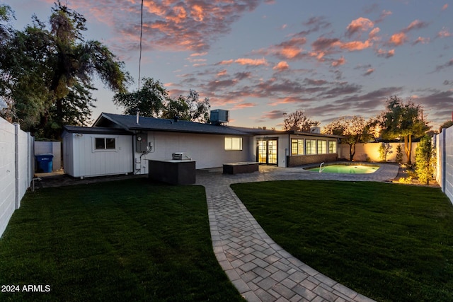 back house at dusk featuring central AC unit, a pool, a yard, and a patio