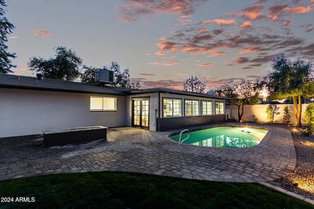 pool at dusk featuring french doors, cooling unit, and a patio area