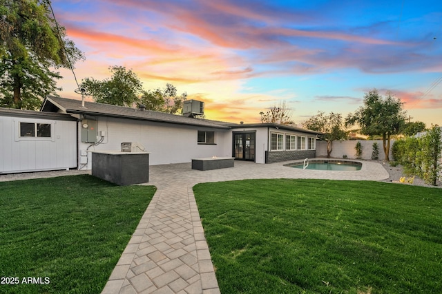 back house at dusk with central AC unit, a patio area, a fenced in pool, and a yard