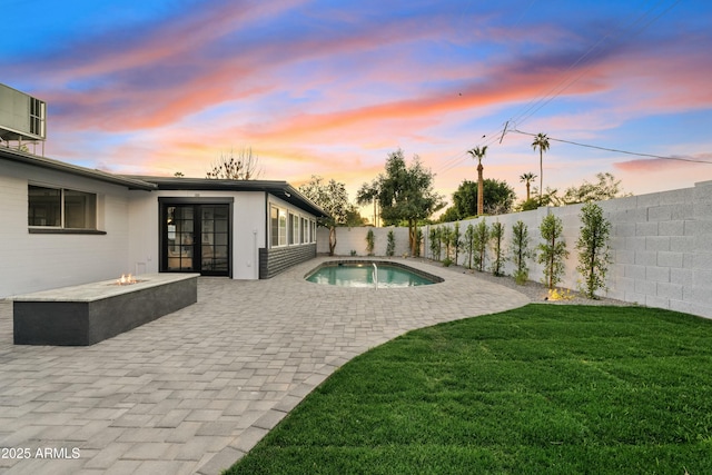 pool at dusk with a patio area, a yard, and an outdoor fire pit