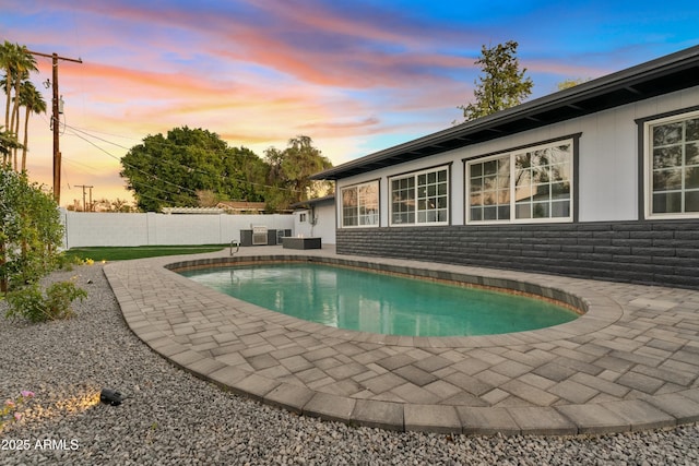 pool at dusk with cooling unit and a patio area