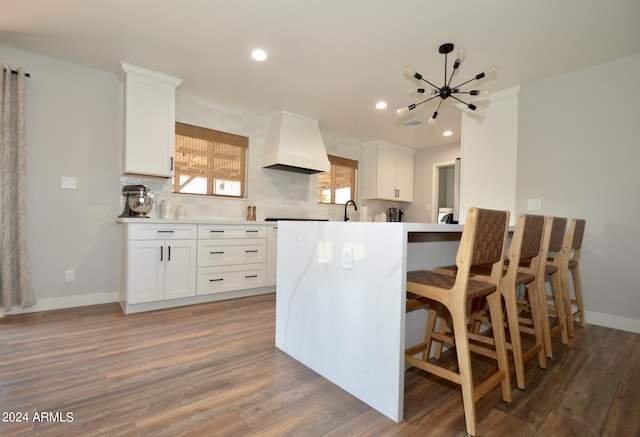 kitchen with hardwood / wood-style flooring, white cabinetry, premium range hood, and decorative backsplash