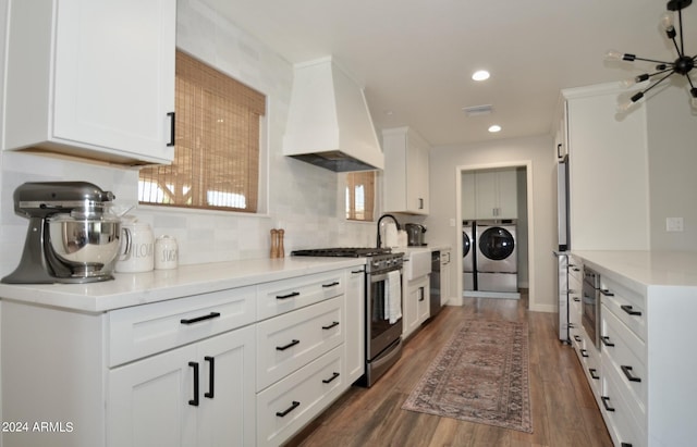 kitchen featuring stainless steel appliances, white cabinetry, custom exhaust hood, washing machine and clothes dryer, and dark wood-type flooring