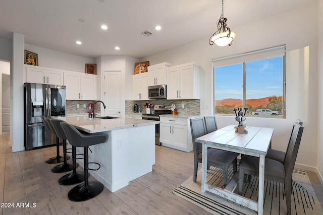 kitchen with appliances with stainless steel finishes, white cabinetry, an island with sink, and sink