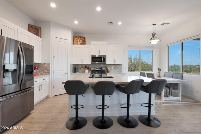 kitchen with decorative light fixtures, stainless steel appliances, an island with sink, white cabinetry, and sink