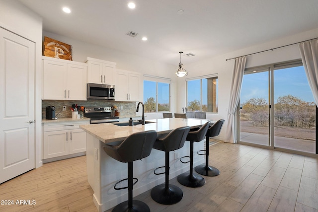 kitchen featuring a center island with sink, decorative light fixtures, white cabinetry, and appliances with stainless steel finishes