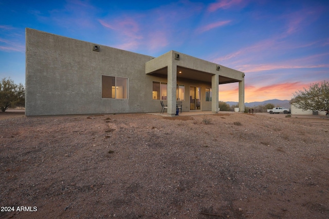 back house at dusk with a mountain view and a patio area