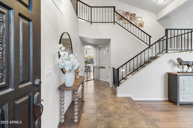 entrance foyer featuring baseboards, stairs, arched walkways, and a high ceiling