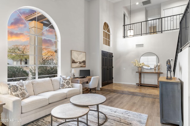 living area with baseboards, a high ceiling, visible vents, and light wood finished floors