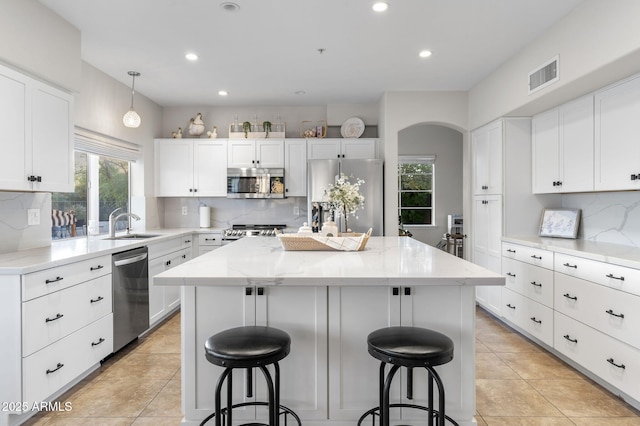 kitchen featuring visible vents, a breakfast bar, light stone countertops, stainless steel appliances, and a kitchen island