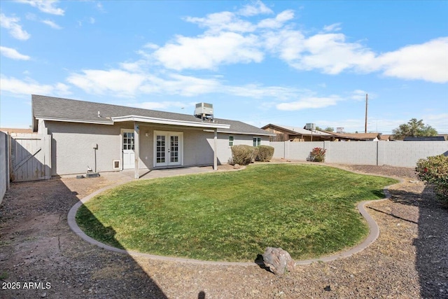 back of house with stucco siding, a fenced backyard, french doors, and a yard