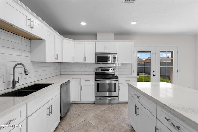 kitchen featuring stainless steel appliances, light stone counters, a sink, and white cabinetry