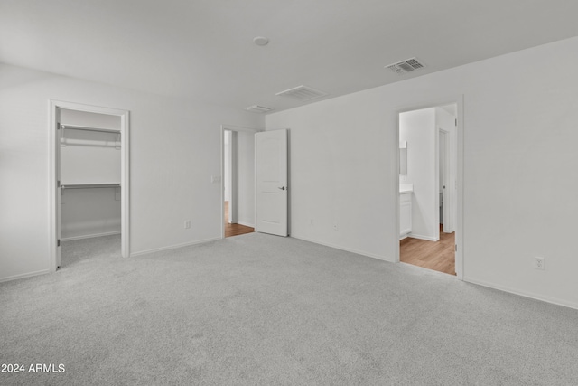 unfurnished bedroom with light carpet, a closet, connected bathroom, and a walk in closet