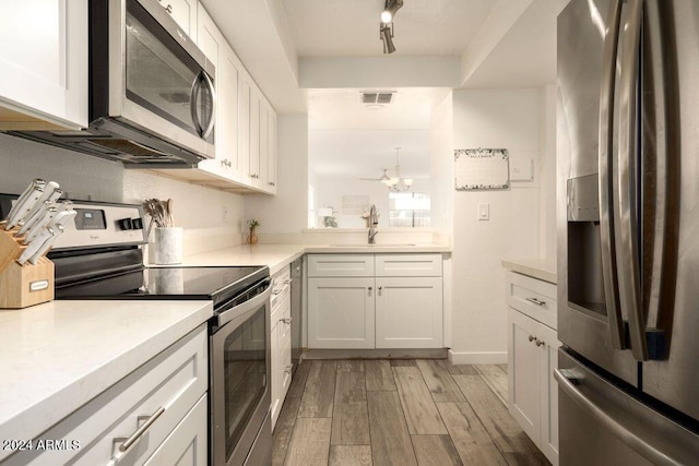 kitchen with appliances with stainless steel finishes, track lighting, sink, light hardwood / wood-style flooring, and white cabinets