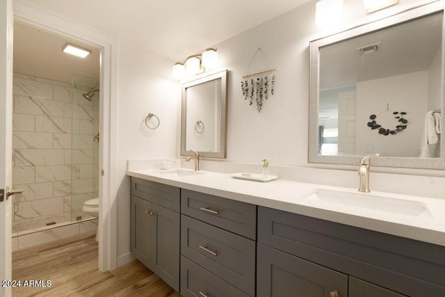 bathroom featuring tiled shower, hardwood / wood-style floors, vanity, and toilet