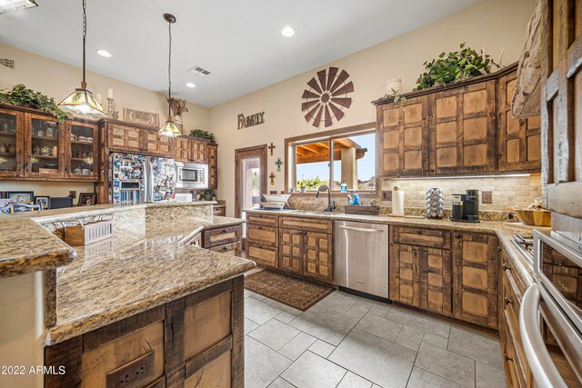 kitchen with light stone countertops, sink, hanging light fixtures, stainless steel appliances, and tasteful backsplash