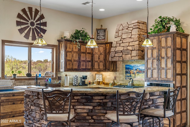 kitchen featuring pendant lighting, tasteful backsplash, stainless steel gas cooktop, and a breakfast bar area