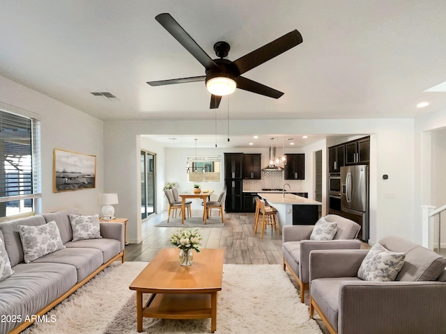 living room featuring ceiling fan with notable chandelier and light hardwood / wood-style flooring