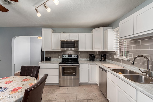 kitchen featuring sink, rail lighting, backsplash, white cabinets, and appliances with stainless steel finishes