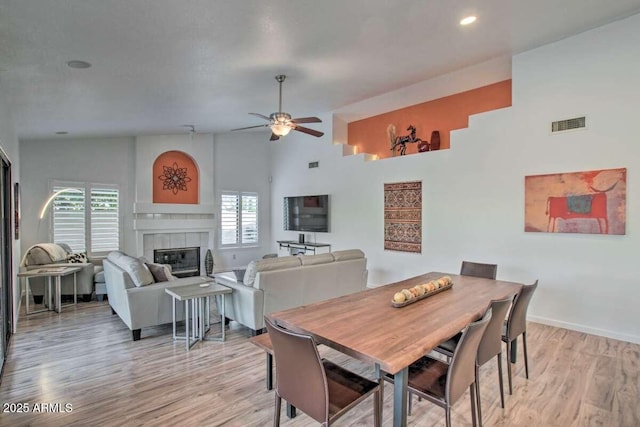 dining room featuring a tiled fireplace, light hardwood / wood-style flooring, high vaulted ceiling, and ceiling fan