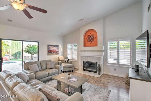 living room featuring ceiling fan, vaulted ceiling, a tile fireplace, and light wood-type flooring