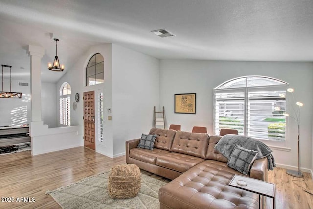 living room with an inviting chandelier, vaulted ceiling, decorative columns, and light wood-type flooring