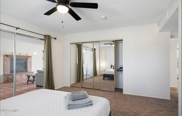 bedroom with a tiled fireplace, ceiling fan, carpet floors, and a textured ceiling