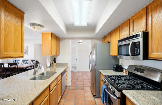 kitchen featuring sink, light stone counters, a tray ceiling, light tile patterned flooring, and appliances with stainless steel finishes