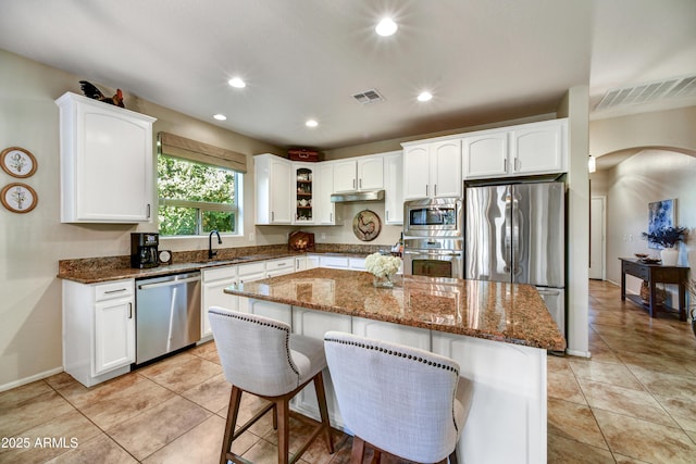 kitchen with stainless steel appliances, a kitchen bar, a kitchen island, and dark stone countertops