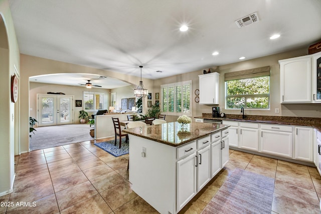 kitchen with a kitchen island, dark stone countertops, white cabinets, hanging light fixtures, and light tile patterned floors