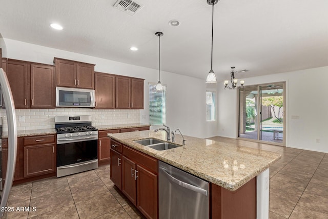 kitchen with pendant lighting, stainless steel appliances, tasteful backsplash, visible vents, and a sink