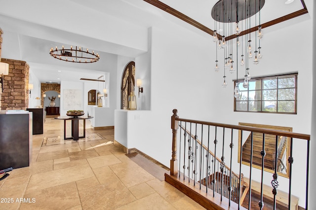 hall with baseboards, arched walkways, an upstairs landing, crown molding, and stone tile flooring