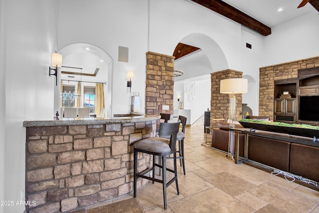 kitchen featuring arched walkways, beam ceiling, stone tile flooring, a high ceiling, and ornate columns