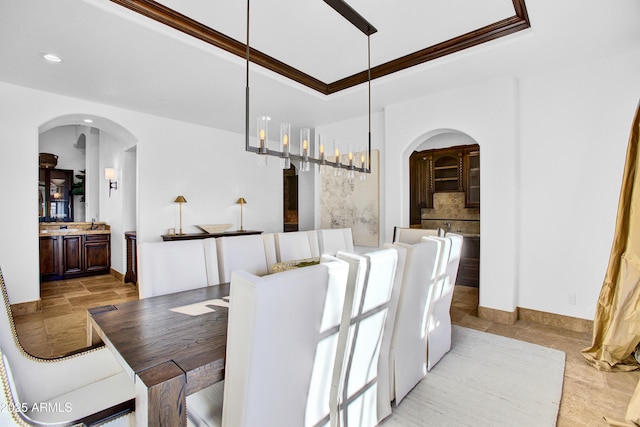 dining space with arched walkways, a tray ceiling, crown molding, recessed lighting, and stone finish flooring