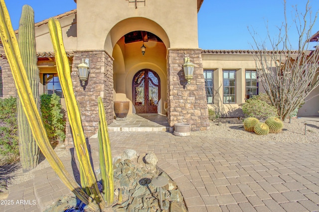 entrance to property featuring stone siding, french doors, and stucco siding