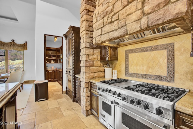 kitchen with decorative backsplash, appliances with stainless steel finishes, light stone countertops, a high ceiling, and stone tile flooring