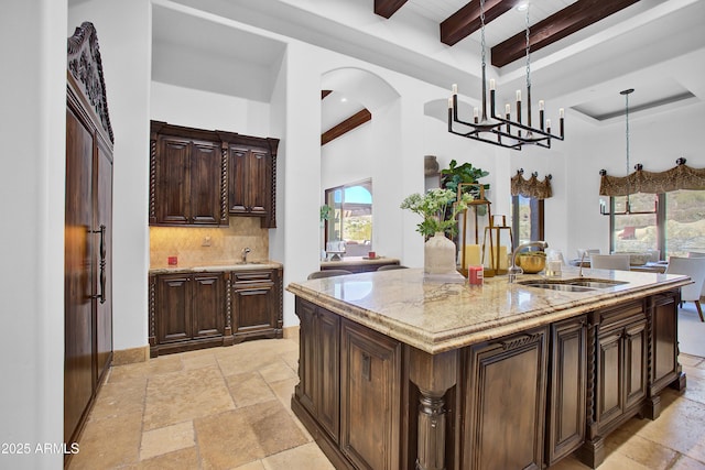 kitchen with stone tile flooring, a sink, hanging light fixtures, and an island with sink