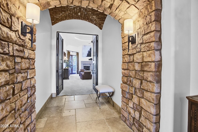 corridor with brick ceiling, stone tile flooring, and baseboards