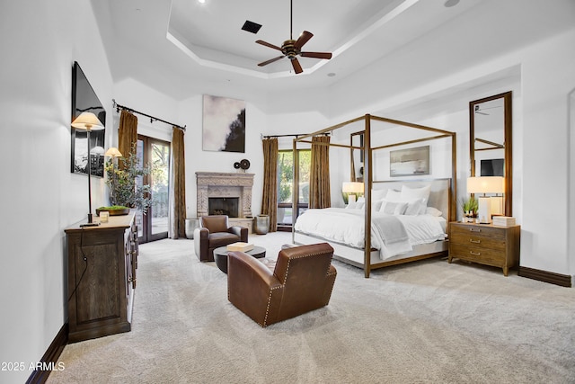 bedroom featuring access to outside, multiple windows, a tray ceiling, and a fireplace with raised hearth