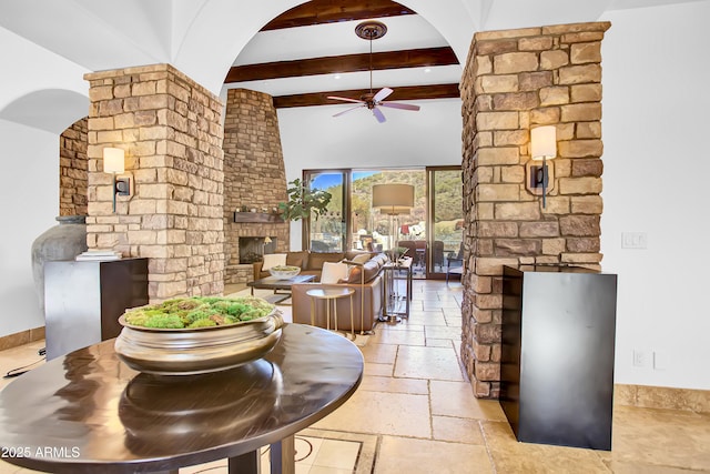 interior space with ceiling fan, arched walkways, a brick fireplace, beamed ceiling, and stone tile flooring