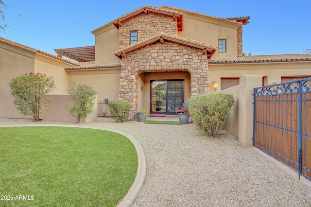 view of front of home featuring a tile roof, stucco siding, a gate, fence, and stone siding